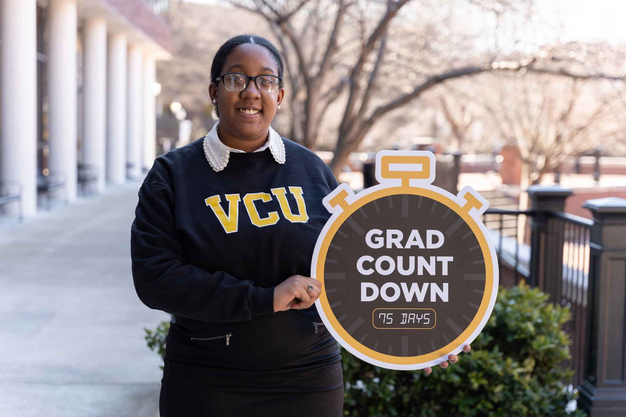 Taylor Jackson holds a Grad Count Down 75 Days sign, shaped like a clock.