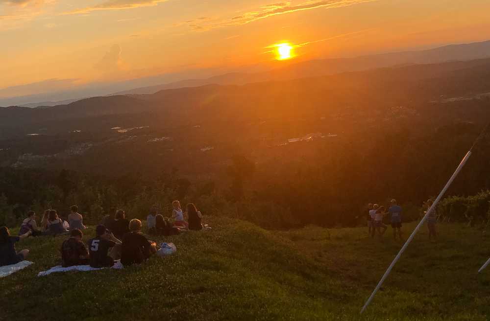 People watch the sunset while sitting on a mountainside.