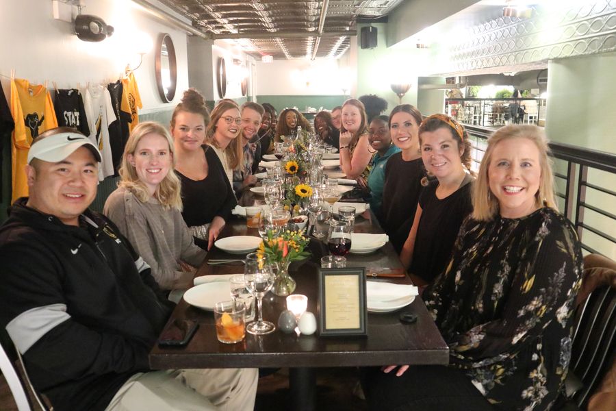 Members of Students Today Alumni Tomorrow smile while sitting down at a large restaurant table.