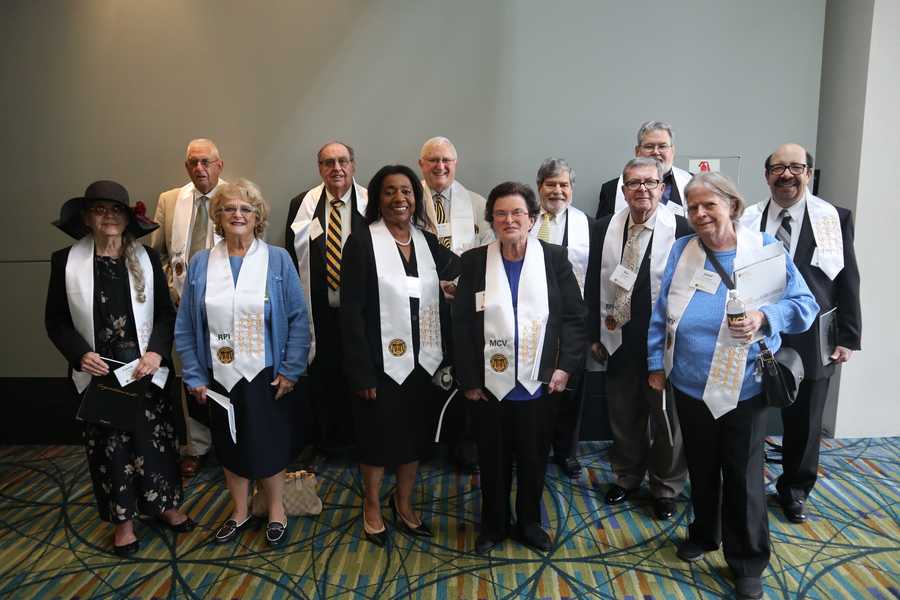 A group of people stand and pose for a photo wearing white graduation stoles.