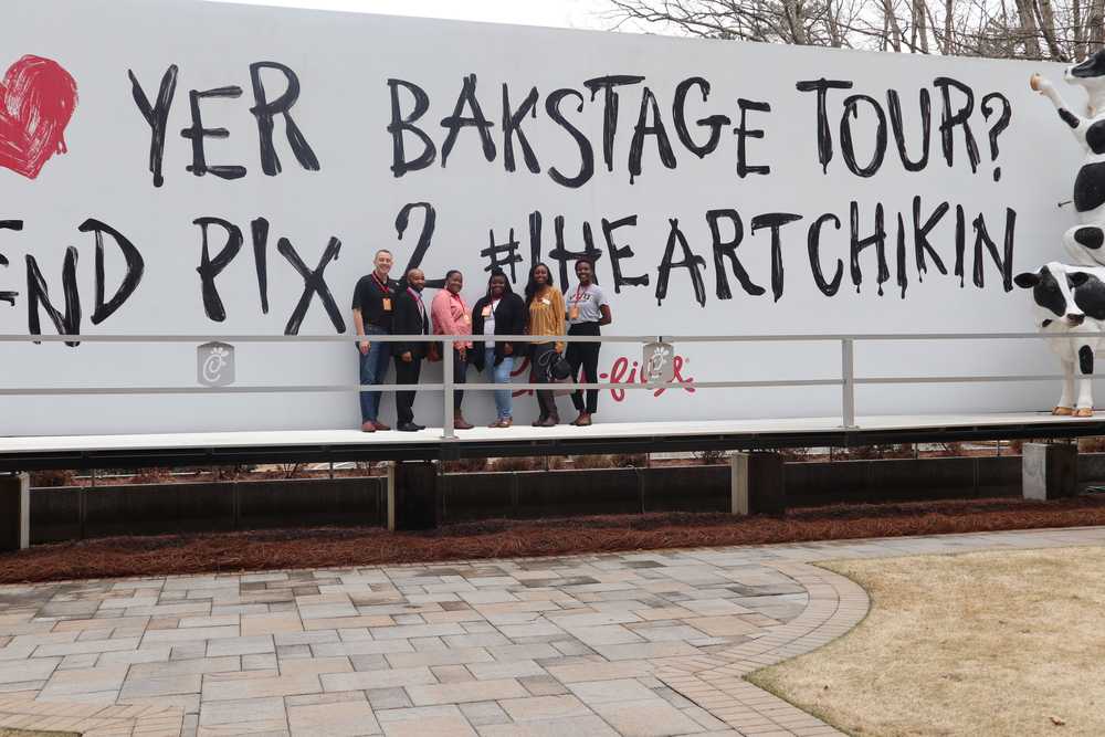 A group of people stand in front of a sign for the Chick-Fil-A headquarters backstage tour.