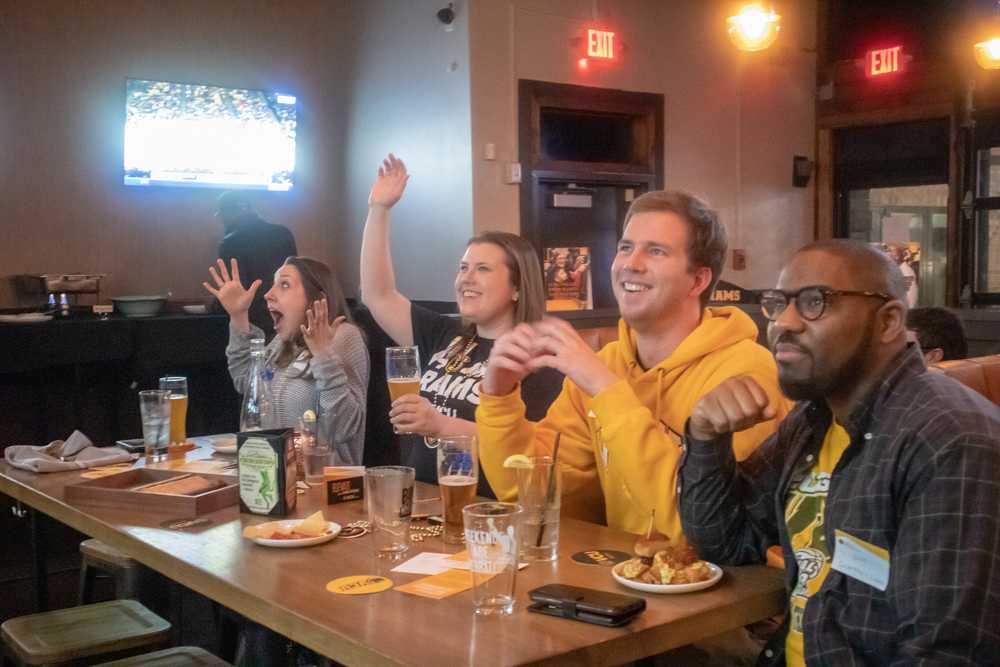 A group of people cheer on a basketball team while at a bar.