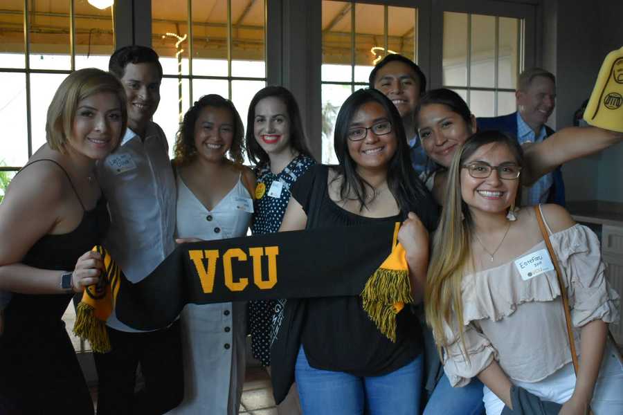 A group of alumni pose for a photo holding a V-C-U branded scarf.