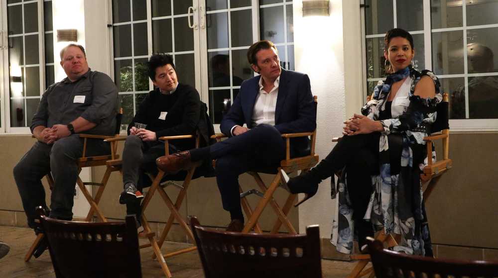 Four alumni panelists sit in chairs at the front of a room.