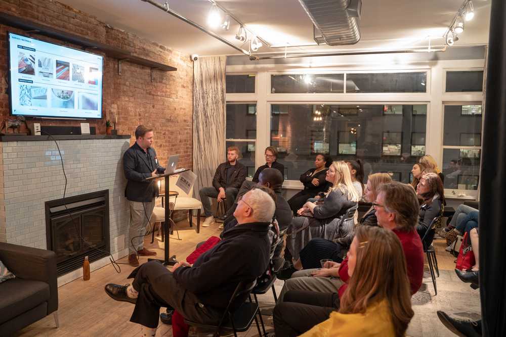 A group of people sit and listen to a speaker talk.