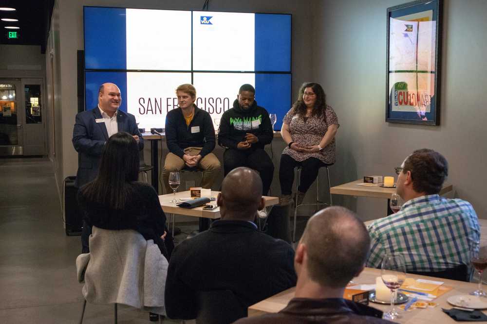 A speaker and three panelists sit at the front of a room before a disussion.