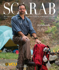 Man standing in a campground holding a red backpack with medical supplies